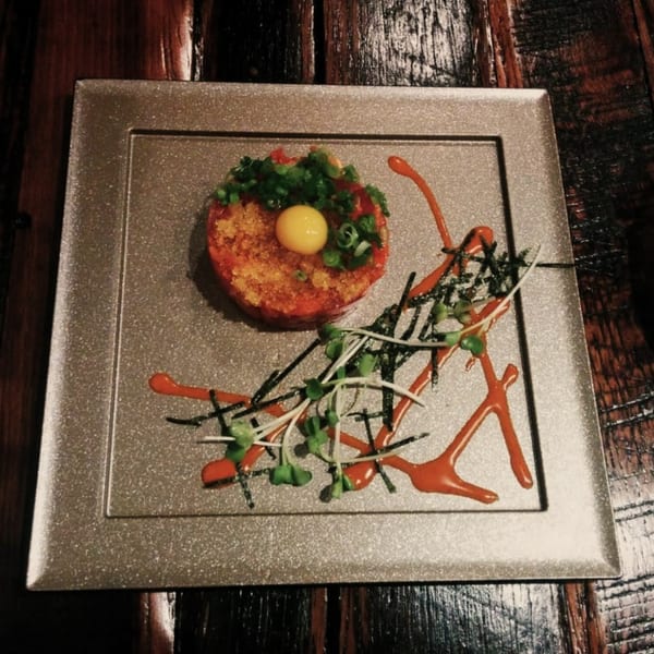 Ginya Izakaya's tuna tartare with a quail egg yolk, green onions, and microgreens on a square plate.