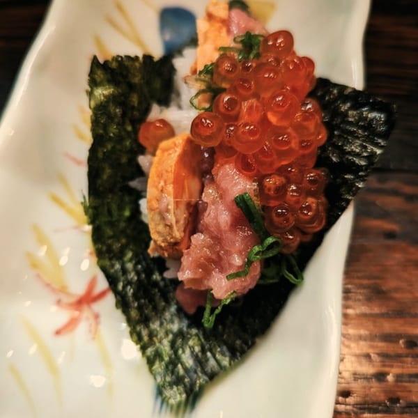 Ginya Izakaya's Japanese hand roll with tuna, salmon roe, and uni on a white plate.