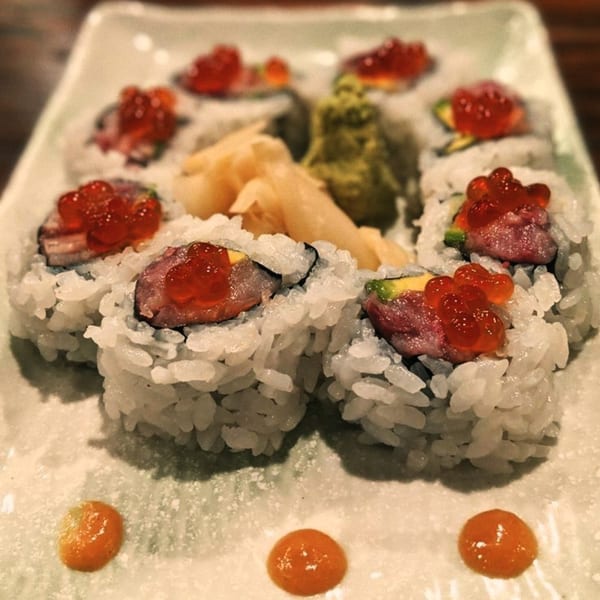 A plate of Ginya Izakaya sushi rolls topped with red roe, served with ginger and wasabi.