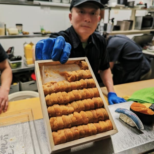 A chef in blue gloves presents a wooden box filled with rows of fresh uni (sea urchin) at Ginya Izakaya.