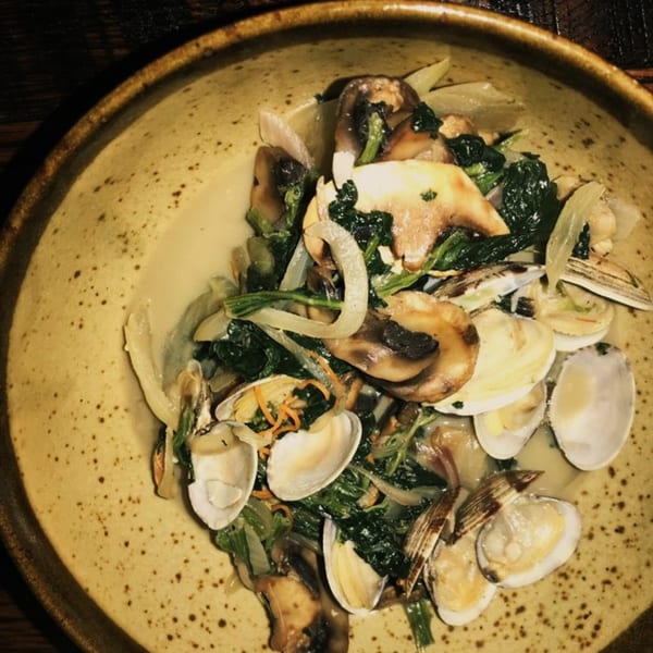 A close-up of a Ginya Izakaya dish with clams, mushrooms, spinach, and onions in a light sauce.
