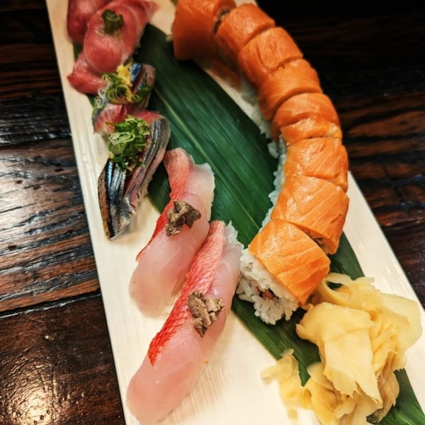 A white platter of Ginya Izakaya sushi and sashimi, including salmon rolls, on a dark wooden table.
